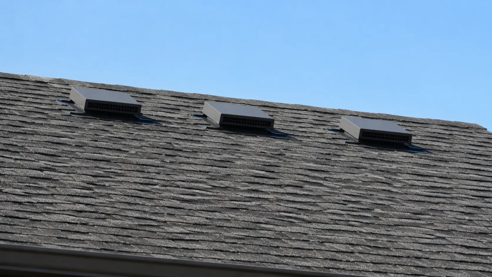 Three box vents spaced along the upper slope of a shingle roof
