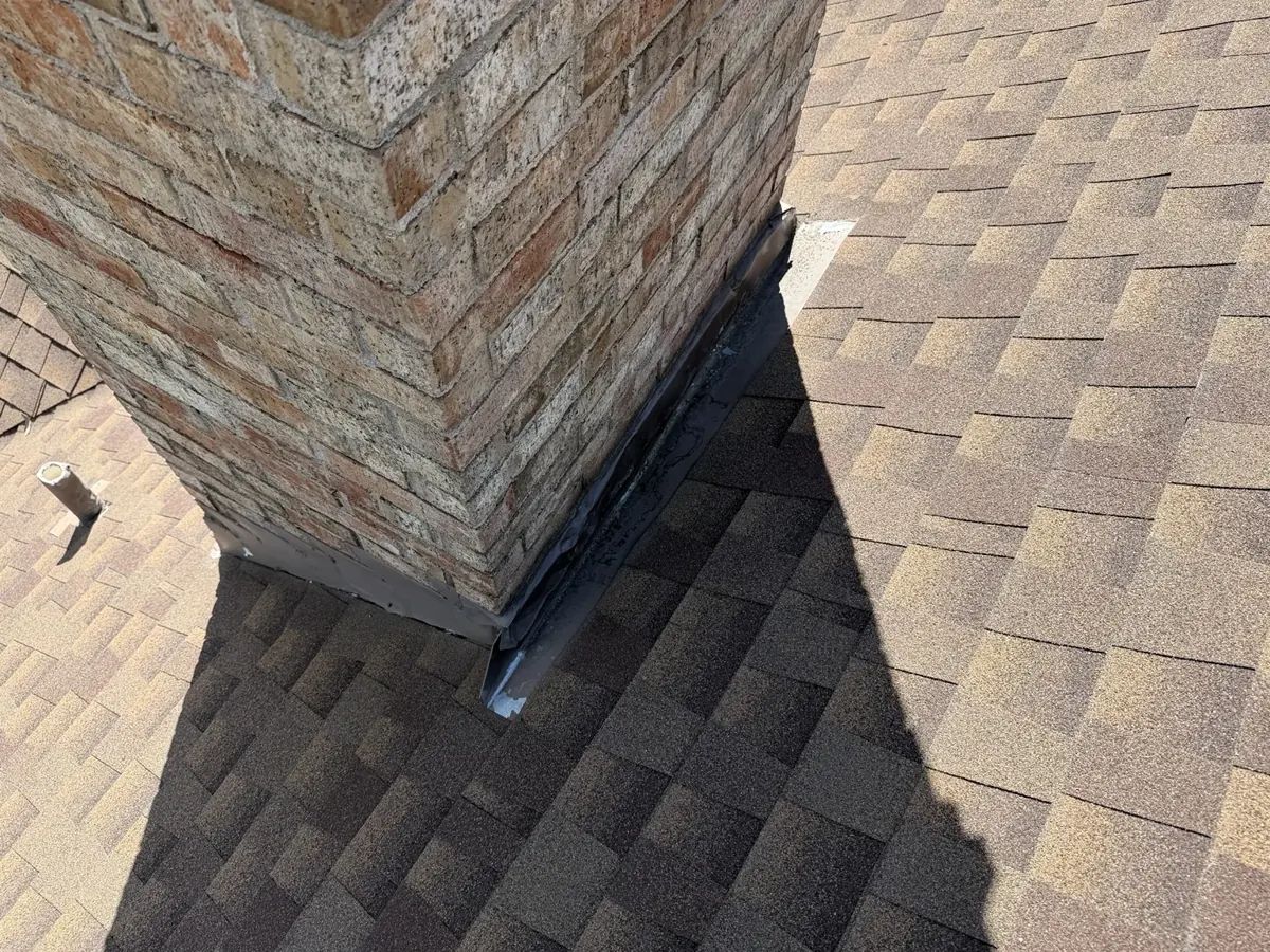 Close-up of flashing around brick chimney and adjoining roof shingles