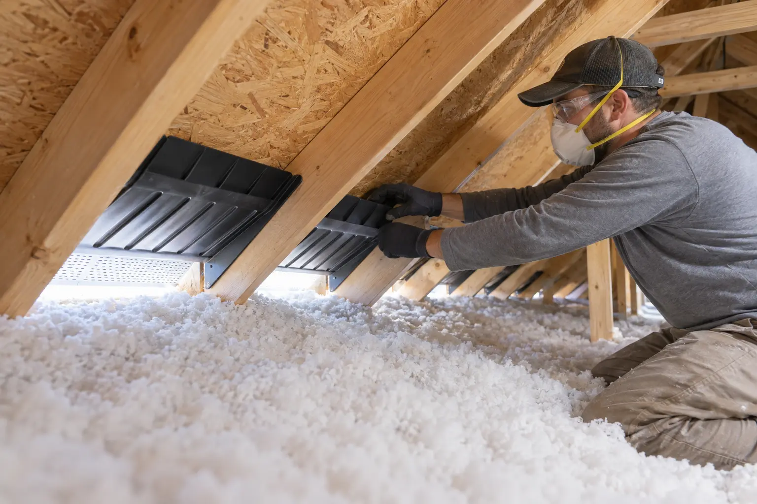 Worker installing ventilation baffles above blown-in attic insulation to keep soffit vents clear